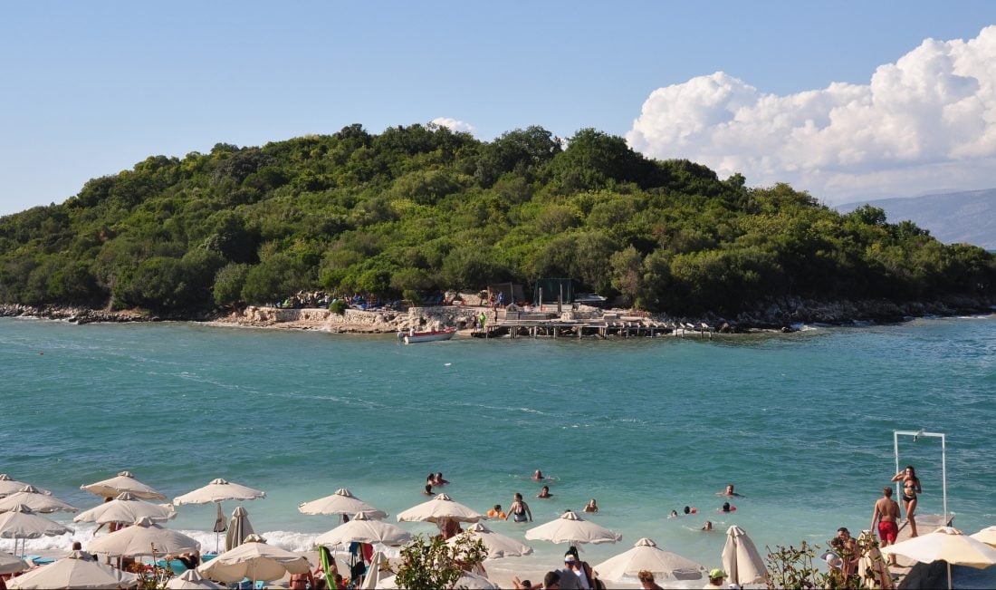 People sitting under umbrellas by the shore of Ksamil Beach