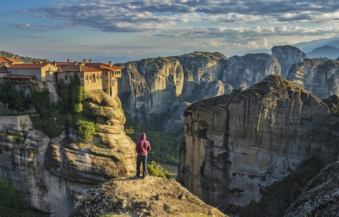 man standing on rocky cliff overlooking a monastery in Meteora Greece