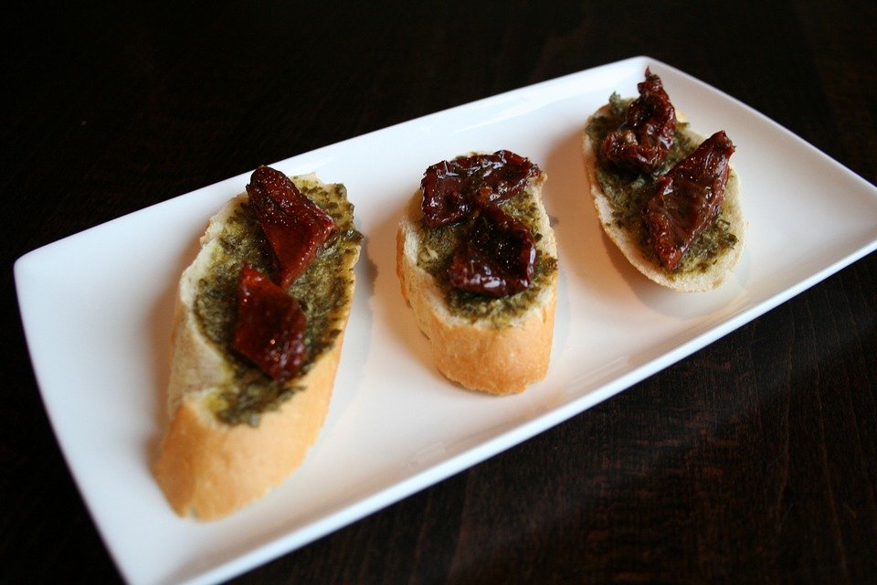 Three pieces of bread with a basil spread and roasted tomatoes on top on a plate in Barcelona