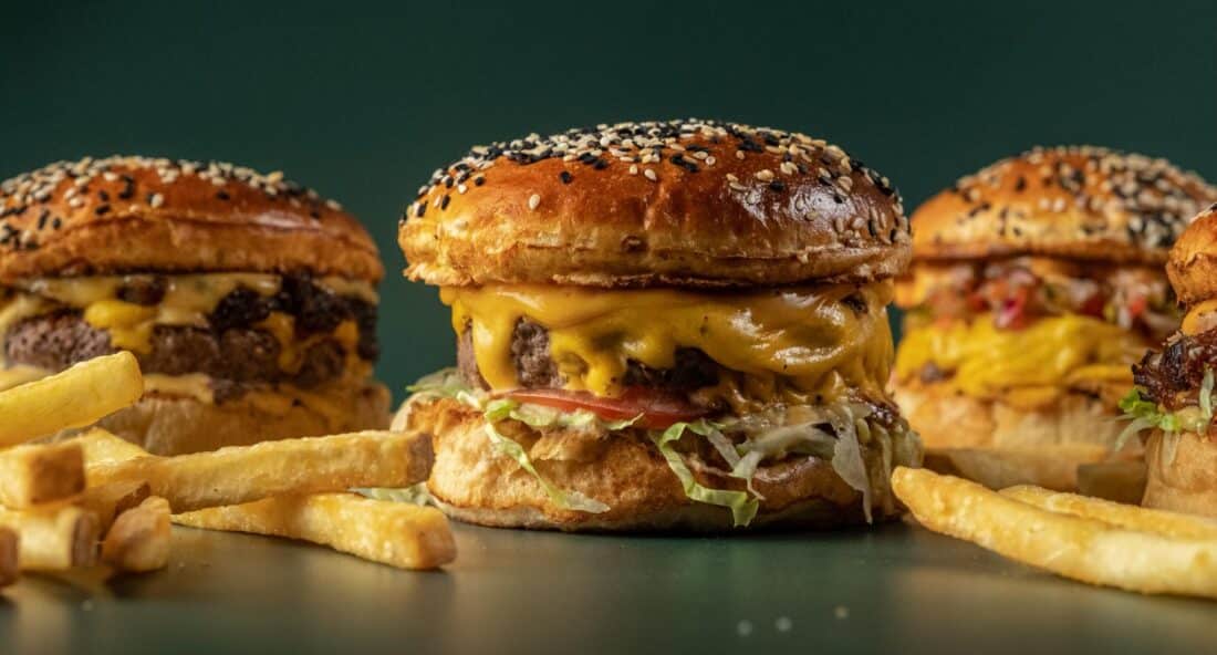 three cheeseburgers on a tray with french fries scattered around