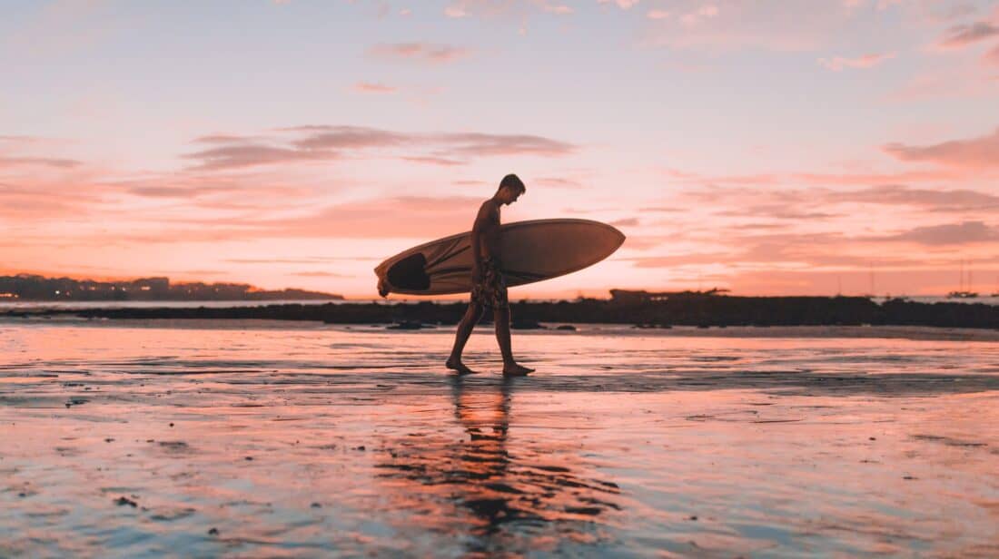 man carrying surfboard on beach in Costa Rica pink sky