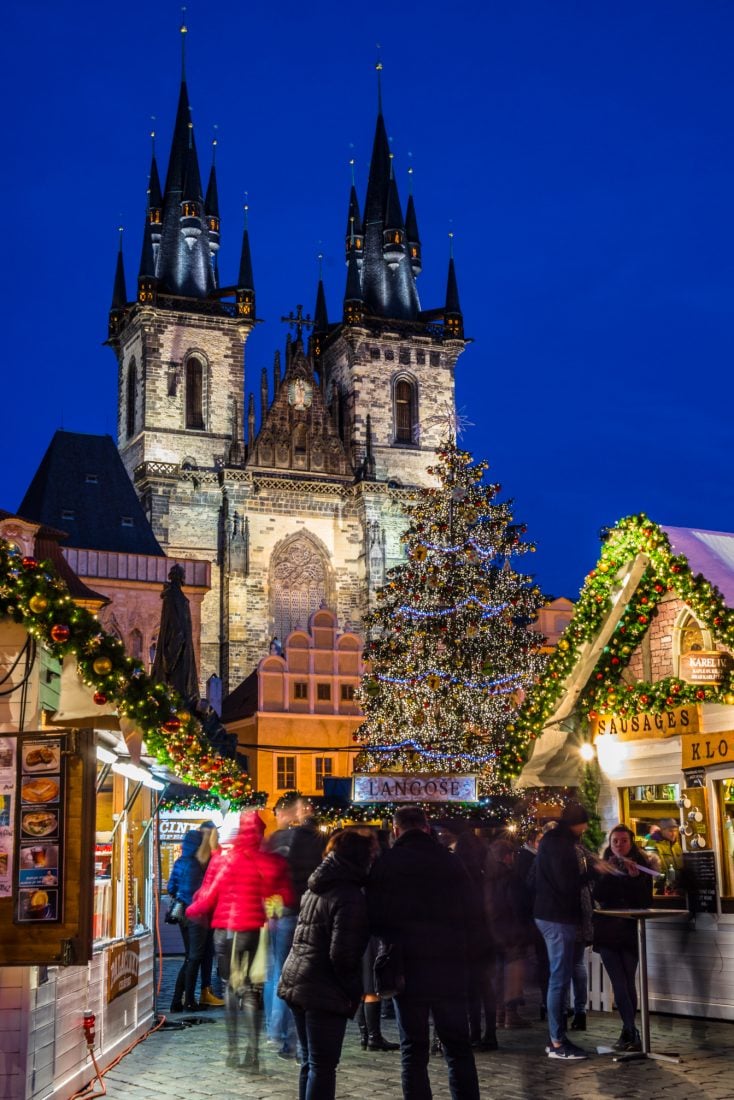 People standing near the Christmas tree in Prague's Old Town Square Christmas Market in the evening.