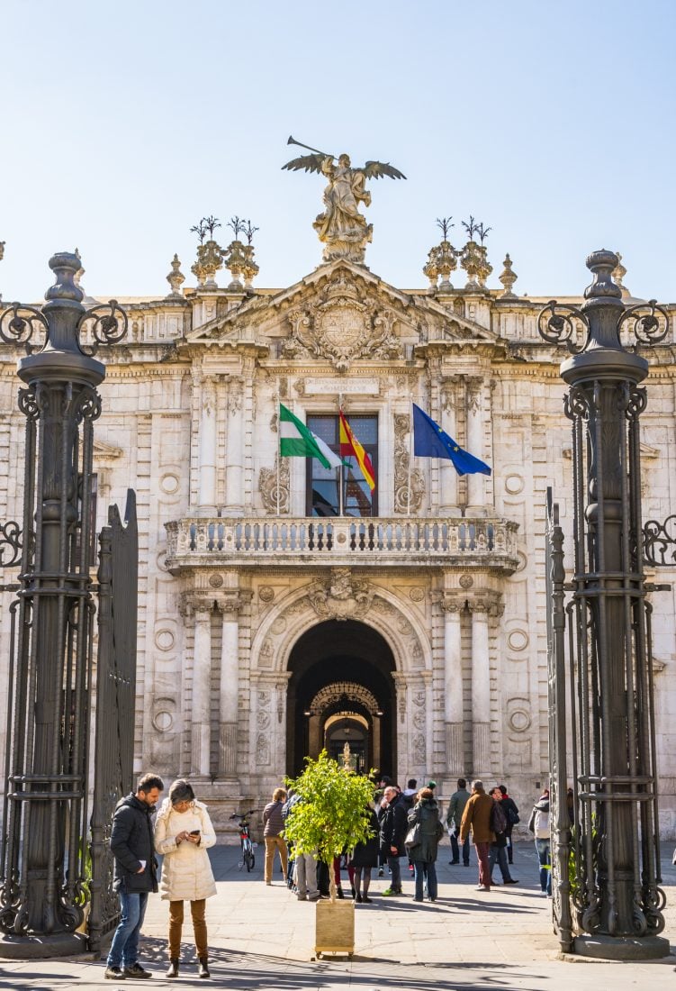 Two people standing in front of the gates to the University of Sevilla.