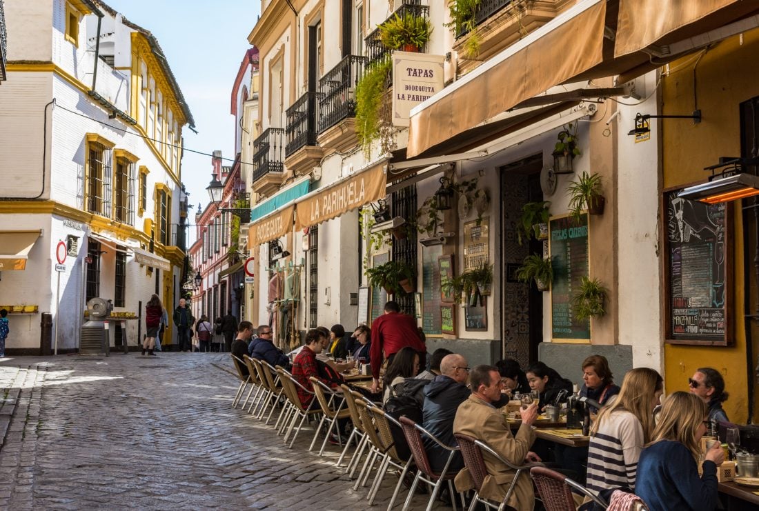 People eating and drinking at small outdoor tables on a street in Sevilla, Spain.