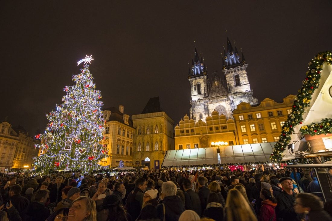 Huge crowd of people in Prague's Old Town Square Christmas Market at night.