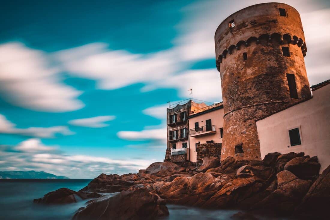 A drum tower and buildings standing above the rocky shore line in Isola del Giglio, Italy.