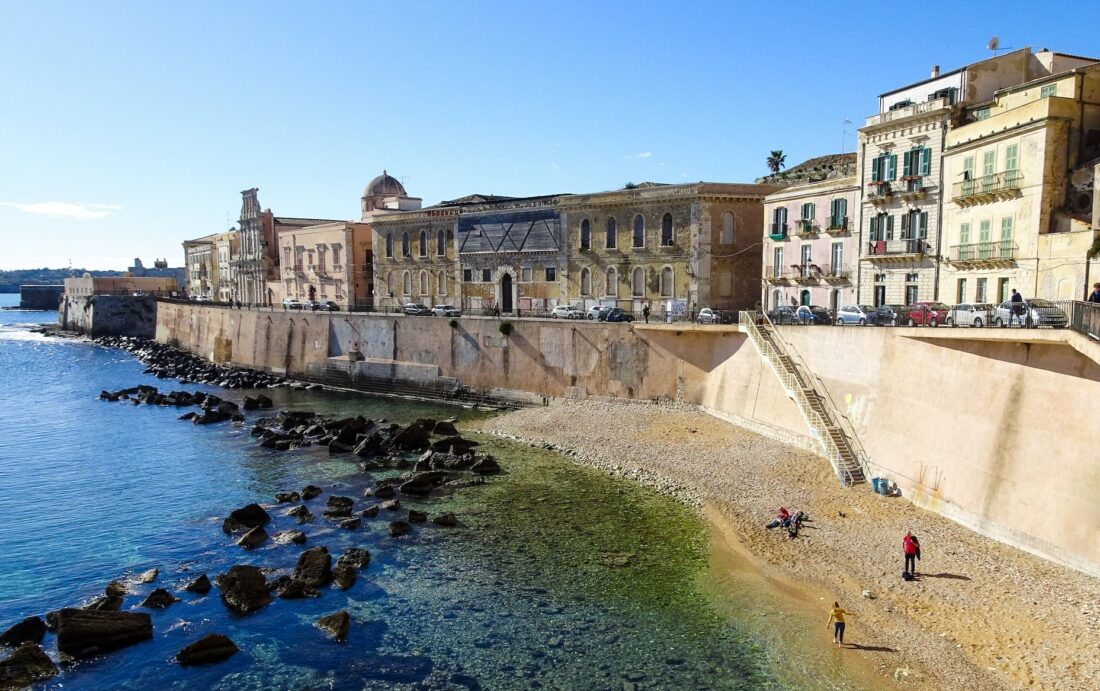 Buildings along a small sea wall on the coastline of Ortigia, Italy.