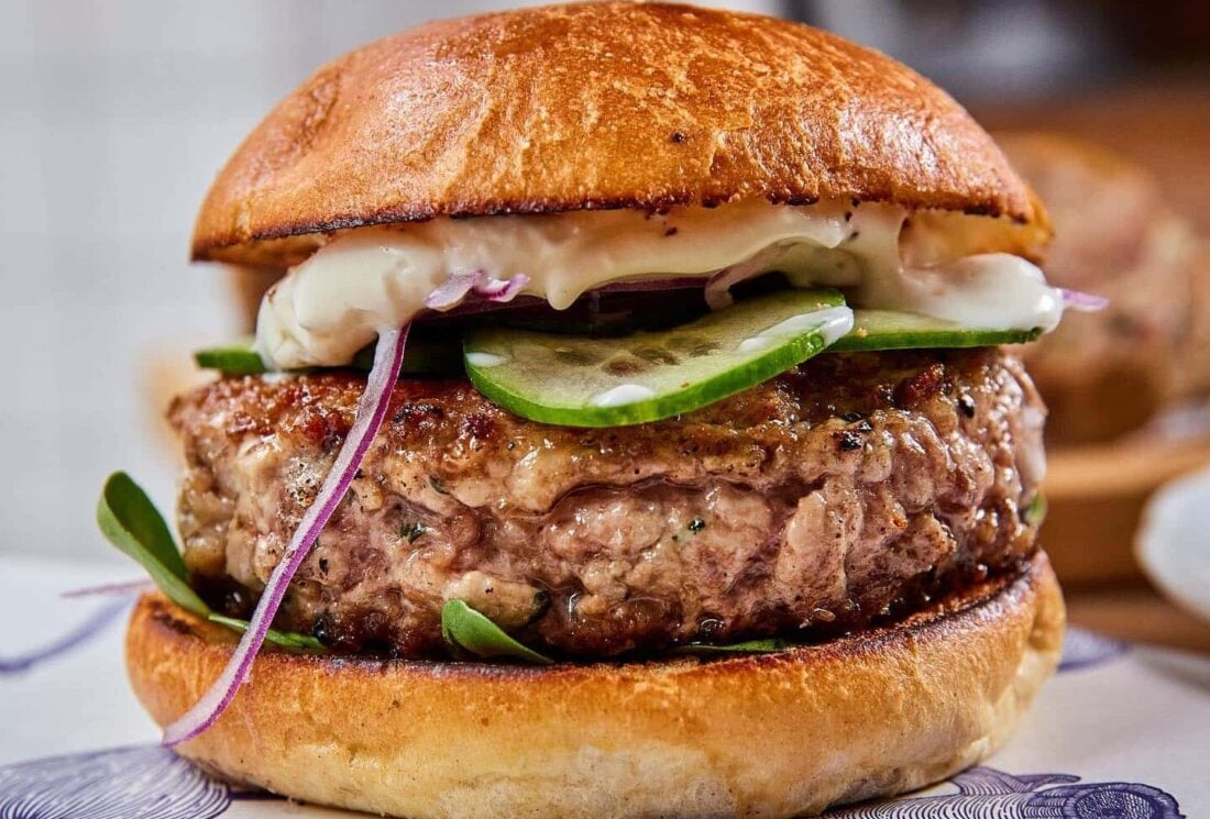 A juicy burger with cucumbers, onions, and sauce.