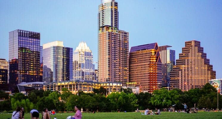 people sitting on grass with Austin skyscrapers behind them