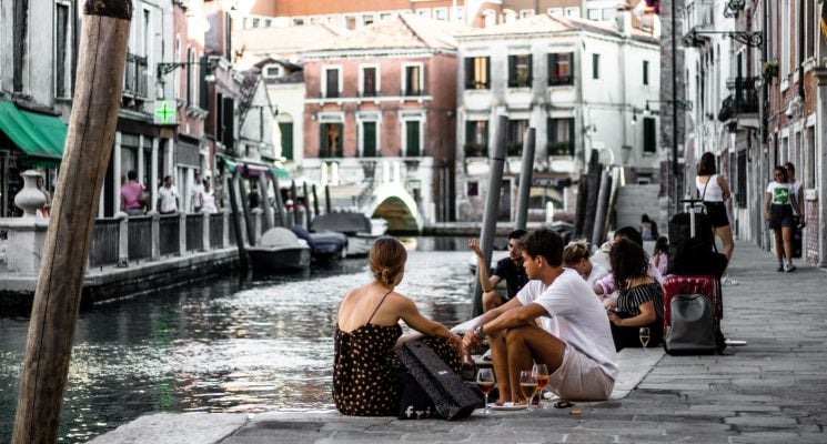 tourists and locals sitting by a canal in Venice Italy