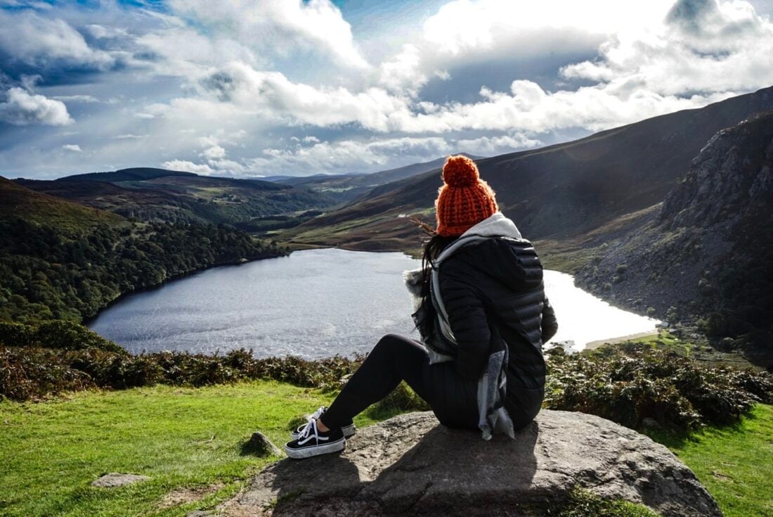 woman sitting on a rock looking at a lake in a valley in Wicklow Ireland